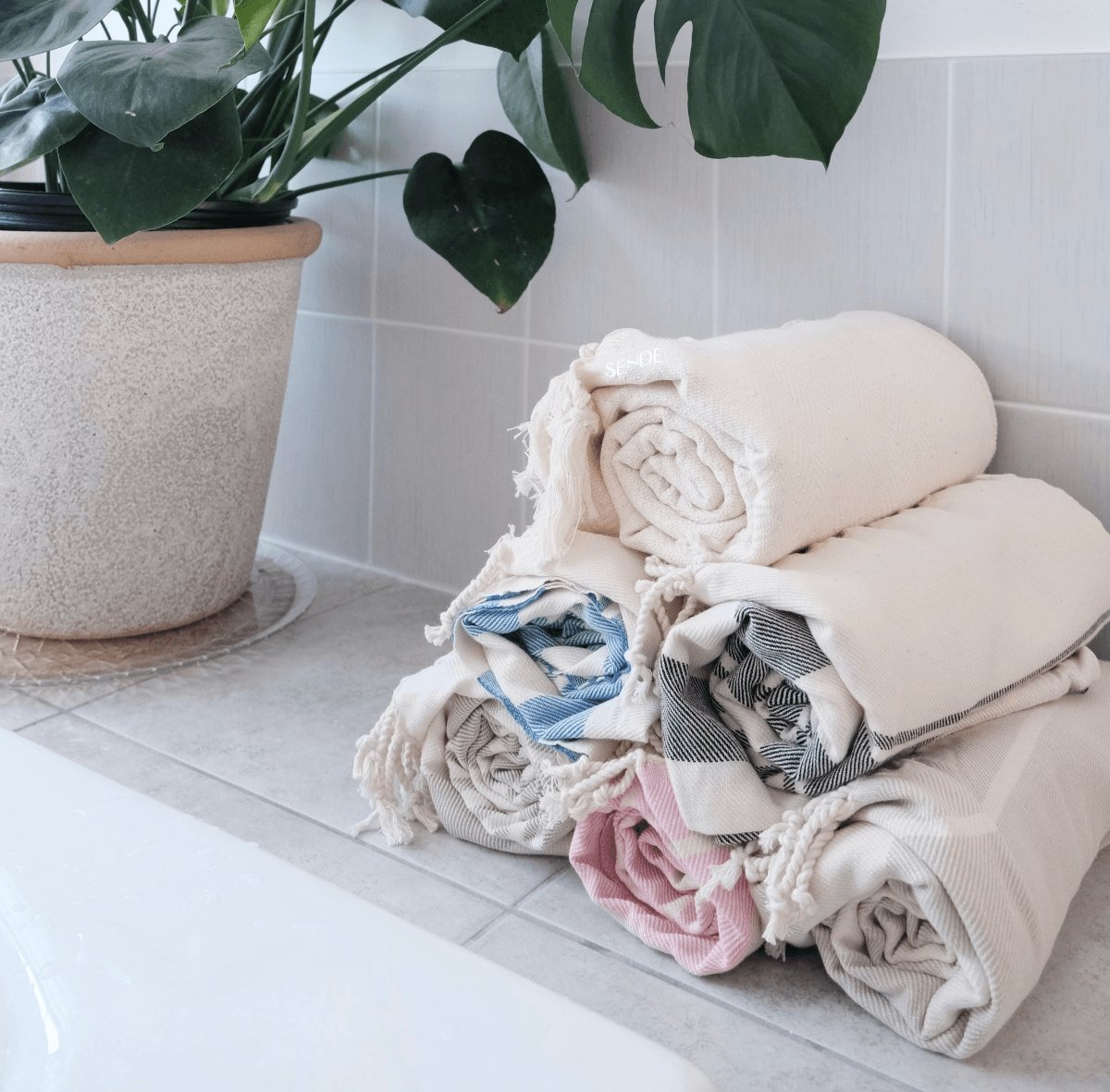 aesthetic rolled towel pyramid in a bright bathroom next to a monstera plant - SENDE