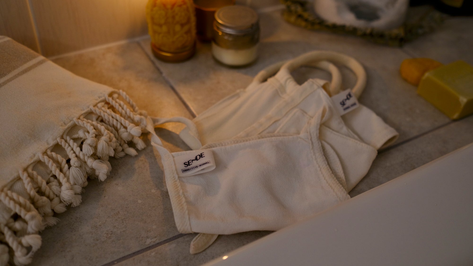 SENDE deep body exfoliating keses by a moody candle-lit bath setup with a Turkish towel, soap and konjac sponge
